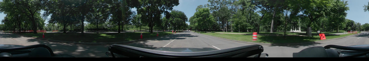 Orange traffic cones line the road as a car drives through Washington, United States, on a clear spring day shaded by lush green trees.