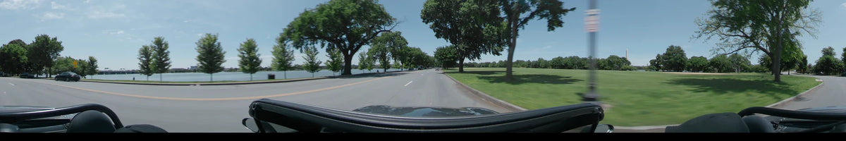 On a clear spring day, a car travels along a road bordered by green trees and a waterfront in Washington, United States.