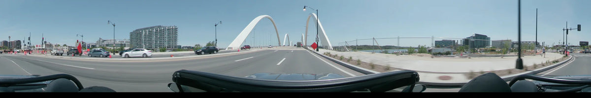 White arches frame the road in Washington, United States, as a car drives past a truck and other vehicles on a clear spring day.