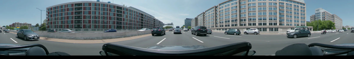 Tall modern buildings flank a multi-lane road in Washington, United States, as a car follows traffic on a clear spring day.