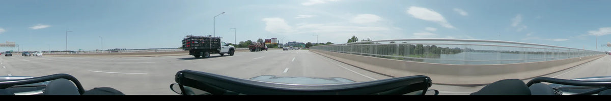 A car travels along a concrete bridge in Washington, United States, passing a flatbed truck and other vehicles on a clear spring day.