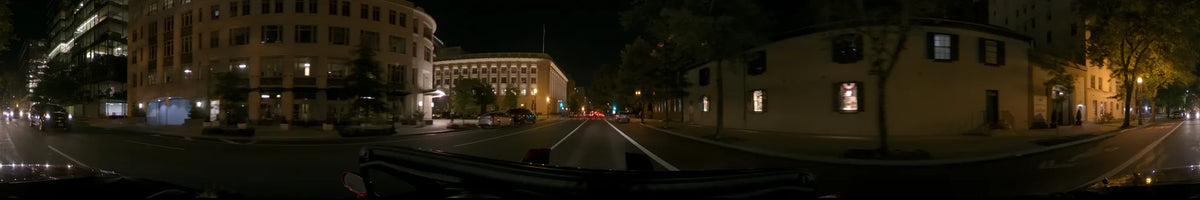 Illuminated neoclassical architecture and city traffic line the road during a clear spring night in Washington, United States, as seen from a moving car.