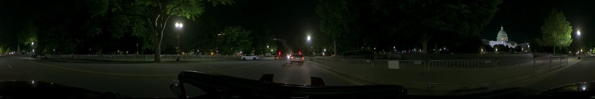 Traveling through Washington, United States, on a clear spring night, a car passes a white vehicle and a white roadside railing beneath glowing streetlamps.
