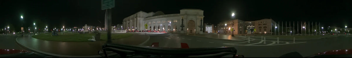 A car travels past the illuminated Union Station in Washington, United States, passing a yellow pedestrian sign and several parked cars on a clear spring night.