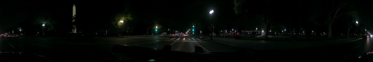 Under glowing streetlamps and green traffic signals, a car approaches a crosswalk and other vehicles in Washington, United States, on a clear spring night.