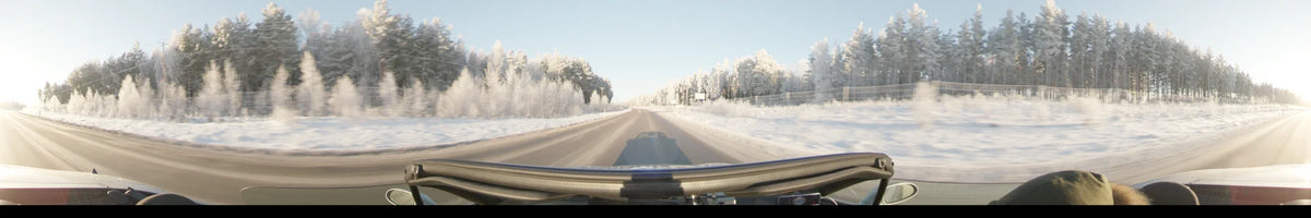 A car drives along a snowy road in Uppsala, Sweden, during a clear winter day, surrounded by frost-covered trees under a bright sky.