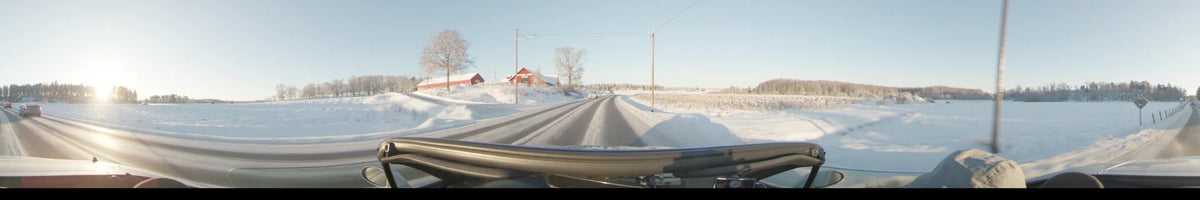 Red wooden buildings and utility poles frame a snow-covered road in Uppsala, Sweden, during a clear winter day seen from a moving car.
