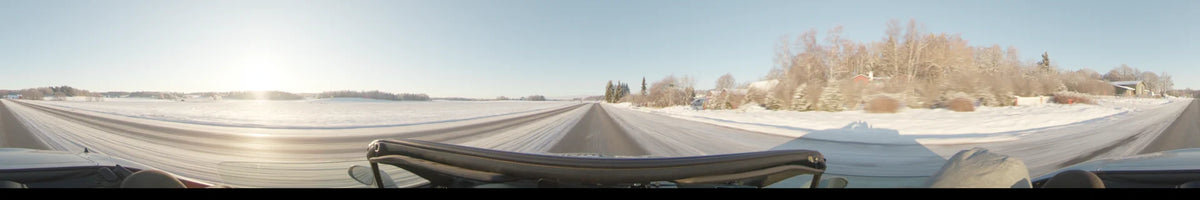 A daytime car journey through Uppsala, Sweden, featuring a snow-covered road flanked by white fields and a few scattered trees under a clear winter sky.