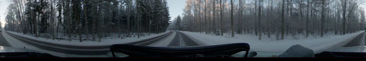 A car moves through a snowy forest in Uppsala, Sweden, on a clear winter day, following a curving road as another vehicle approaches from ahead.