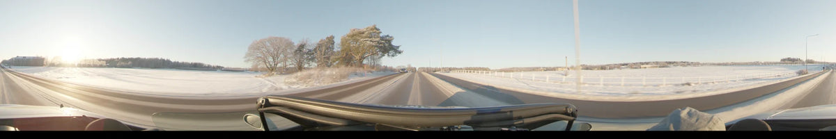 Seen from a car, a snowy road in Uppsala, Sweden, stretches forward past frost-covered trees and a white guardrail under a clear winter sky.
