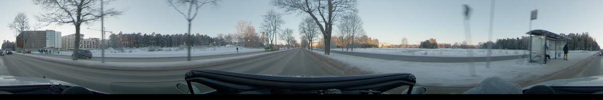 Passing a green bus and bare trees, a car travels along a snowy road in Uppsala, Sweden, during a clear winter day.