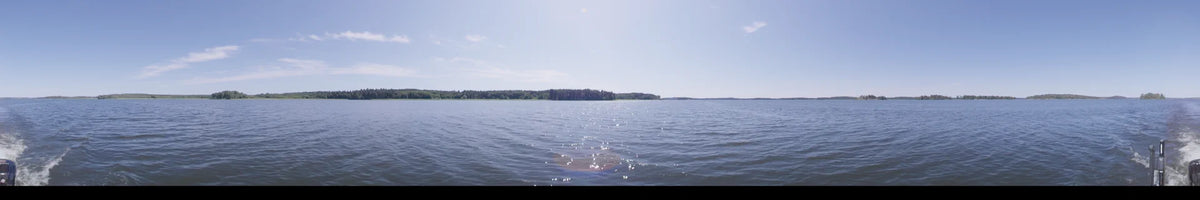 Sunlight glitters across the lake in Upplands-Bro, Sweden, during the day. From a boat, a distant forested shoreline is visible under a clear summer sky.