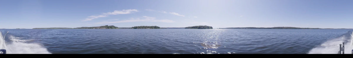 Shimmering water and distant green forests fill the view from a boat in Upplands-Bro, Sweden, under a clear summer sky during the day.