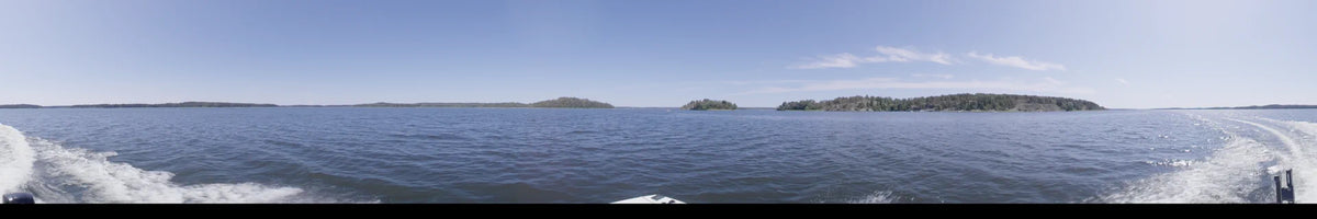 Several small, forested islands appear on the horizon in Upplands-Bro, Sweden. The daytime scene is captured from a boat under a clear summer sky.