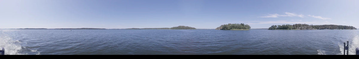 Captured from a boat in Upplands-Bro, Sweden, this daytime scene shows a vast water surface and distant wooded shores under a clear summer sky.