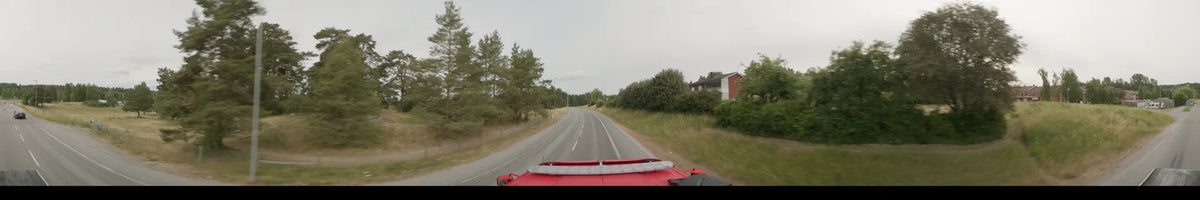 Passing a red house and thick woodland, a red bus travels a curving road in Märsta, Sweden, during an overcast summer morning.