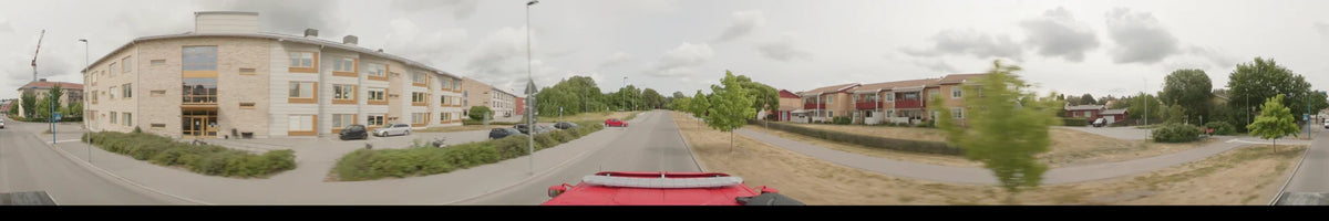 On an overcast summer morning in Märsta, Sweden, a bus travels a straight road bordered by green trees and houses.