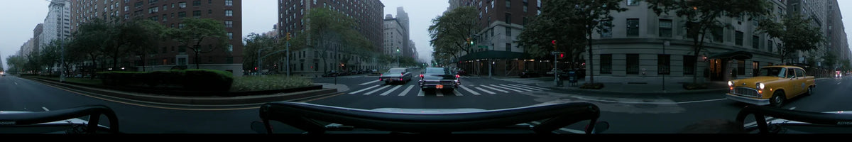A morning drive through New York City during spring. Vintage cars travel along East 73rd Street under an overcast sky, flanked by tall brick buildings.