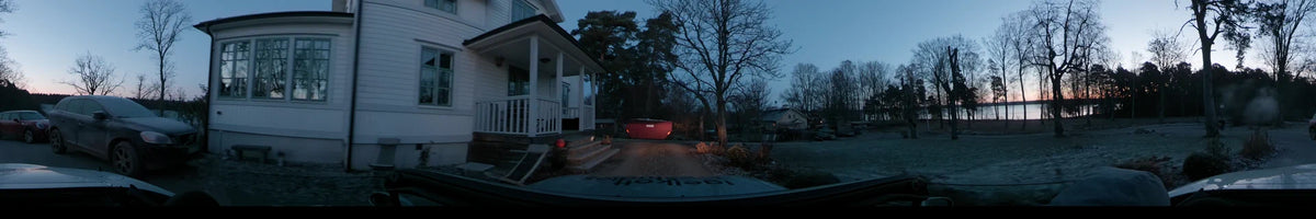 A car driving through Lennartsnäs, Sweden, on a clear autumn morning. The view features a white wooden house and a red container on a gravel path.
