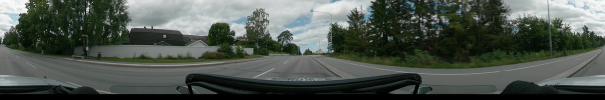 A multi-lane road in Uppsala is lined with lush green trees, streetlights, and a few distant houses under a partly cloudy sky.
