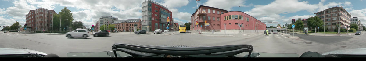 A yellow bus drives ahead on a street in Uppsala, flanked by red and grey buildings, parked cars, and a person on a scooter.