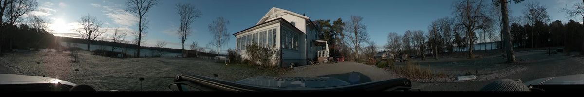 A clear autumn day in Lennartsnäs, Sweden. The shot from a car shows a white wooden house with a glassed-in porch next to a gravel path.