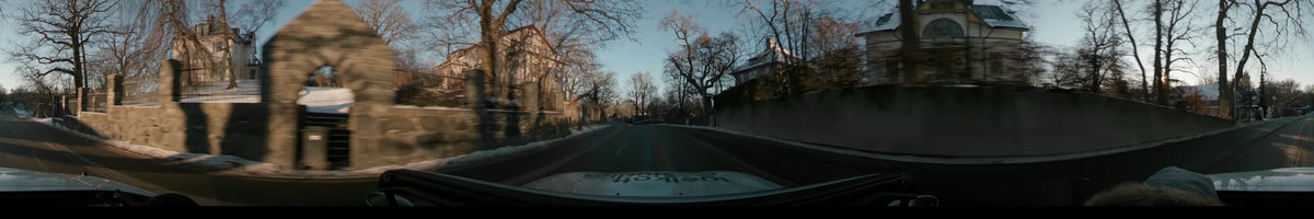Houses and leafless trees pass by as a car travels through a neighborhood in Stockholm, Sweden, during a clear winter sunset.