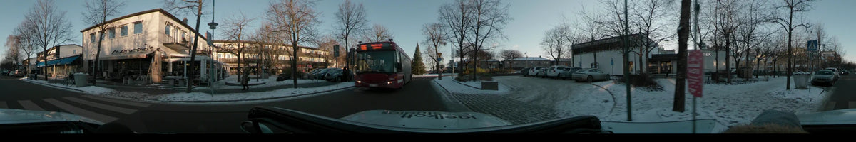 A red bus and leafless trees flank a snowy street in Stockholm, Sweden, as a car travels through the city under a clear winter sunset.