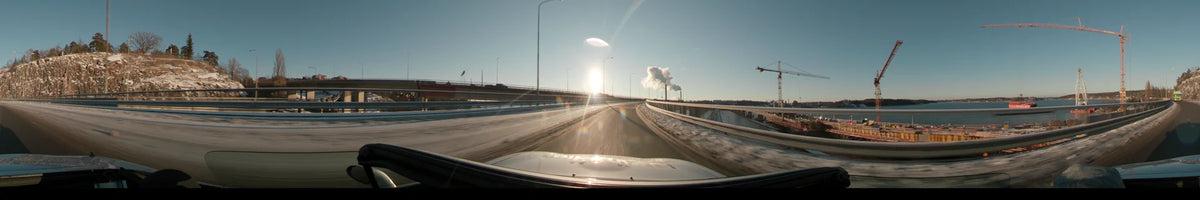 Under a clear winter sunset, a car travels across a highway bridge in Stockholm, Sweden, passing snow-covered edges and distant industrial smoke.