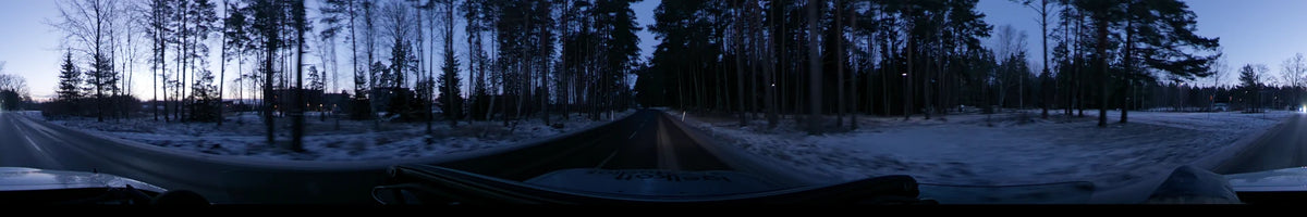 A car travels along a road through a snowy pine forest in Stockholm, Sweden, under a clear sky during a winter dawn.