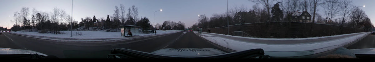 Under a clear winter dawn sky, a car passes a bus stop and pedestrians on a snowy road in Stockholm, Sweden.