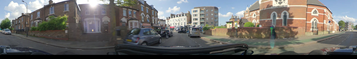 Brick storefronts and a modern apartment building line a street in London, United Kingdom, as a car drives by during a partly cloudy spring day.