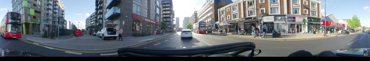 On a clear spring day in London, United Kingdom, a car follows a white vehicle past a red double-decker bus and a Costa Coffee storefront.
