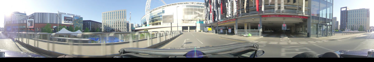 The modern architecture of the Tottenham Hotspur Stadium looms ahead as a car drives through London, United Kingdom, on a clear spring day.