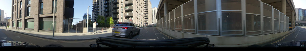 Modern brick apartments and a concrete overpass flank a road in London, United Kingdom, where a car drives on a clear spring day.