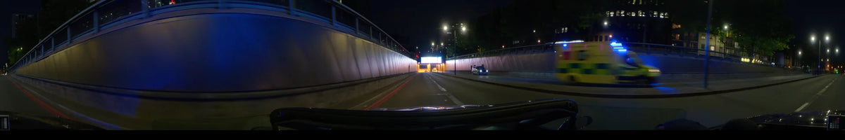 A car drives through a concrete underpass at night in London, United Kingdom. Bright street lights and an illuminated overhead sign light up the road.