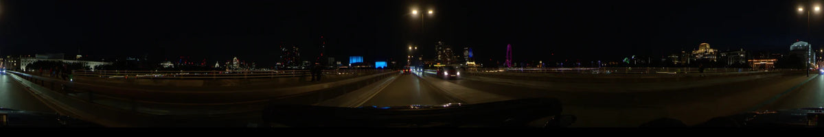 The purple London Eye and city skyline frame a nighttime car journey through London, United Kingdom, during spring, as other vehicles travel along the road.