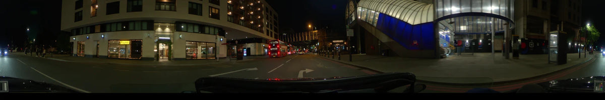 The Minories and red double-decker buses appear along a city road in London, United Kingdom, as a car moves through a clear spring night.