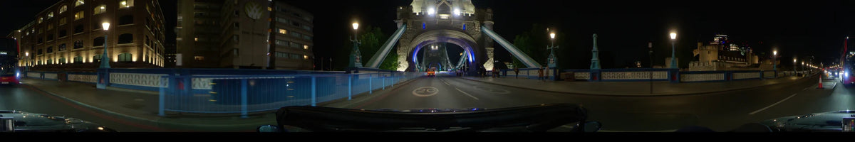 Tower Bridge is illuminated as a car drives through London, United Kingdom, on a clear spring night, passing pedestrians along the road.