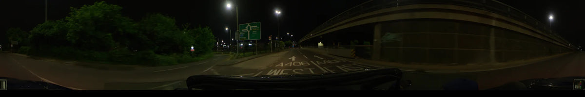 A car travels along the A406 North Circular Road in London, United Kingdom, on a clear spring night, passing a large directional sign beneath a concrete overpass.