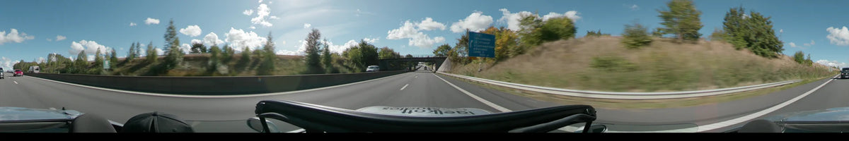 A highway in Lund passes under a concrete bridge and past a blue road sign, with autumn trees and other vehicles visible under a clear sky.
