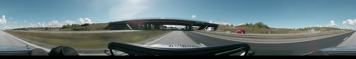 A highway overpass crosses a multi-lane road between Lund and Malmö, with a white camper van driving alongside in the right lane under a clear sky.