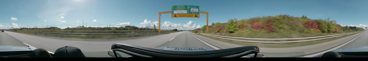 A highway in Malmö features a large overhead road sign directing traffic toward Copenhagen and Limhamn, flanked by autumn foliage under a clear sky.