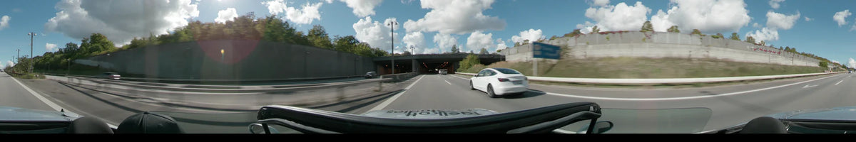 A highway with a white car and a van passes under a concrete bridge between Malmö and Copenhagen under a clear sky.