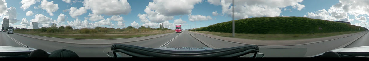 A red truck drives on a multi-lane highway lined with green hedges and street lamps in Copenhagen under a partly cloudy sky.