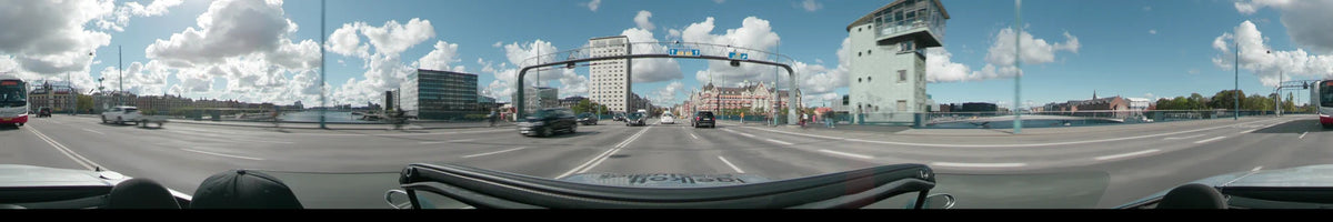 A wide city road in Copenhagen featuring a tall white office building and ornate red brick architecture under a partly cloudy sky with moderate traffic.