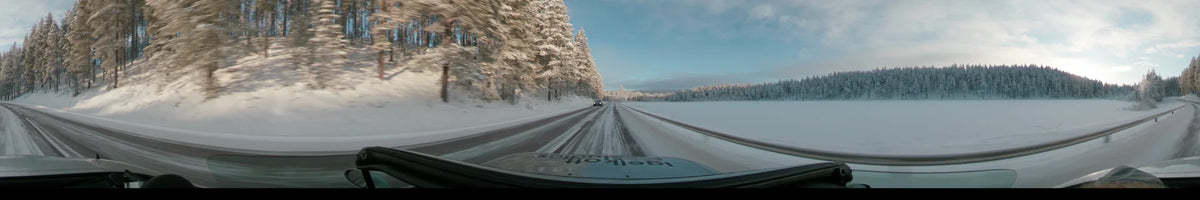 A car follows another vehicle on a snowy road in Dalarna, Sweden, flanked by frost-covered trees and open fields during a partly cloudy winter day.