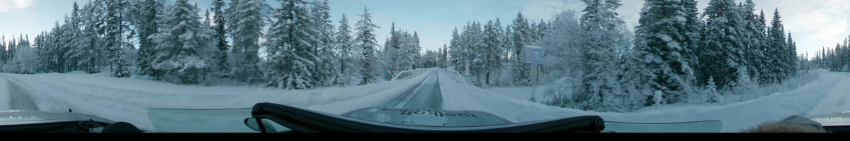 During a partly cloudy winter day in Dalarna, Sweden, a car crosses a snow-covered bridge amidst dense, frost-laden pine trees.