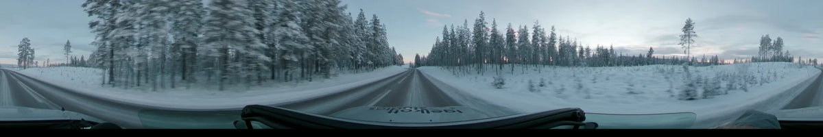A snowy road stretches through a forest of snow-covered trees in Dalarna, Sweden, seen from a car on a partly cloudy winter afternoon.