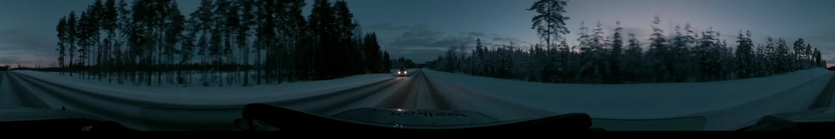 Passing other vehicles, a car moves along a snowy road through winter forests in Dalarna, Sweden, under a partly cloudy twilight sky.